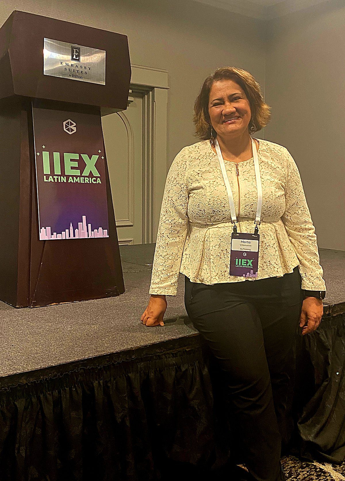 Marta Villanueva on stage at IIEX Latin America, standing
                      beside the event podium.