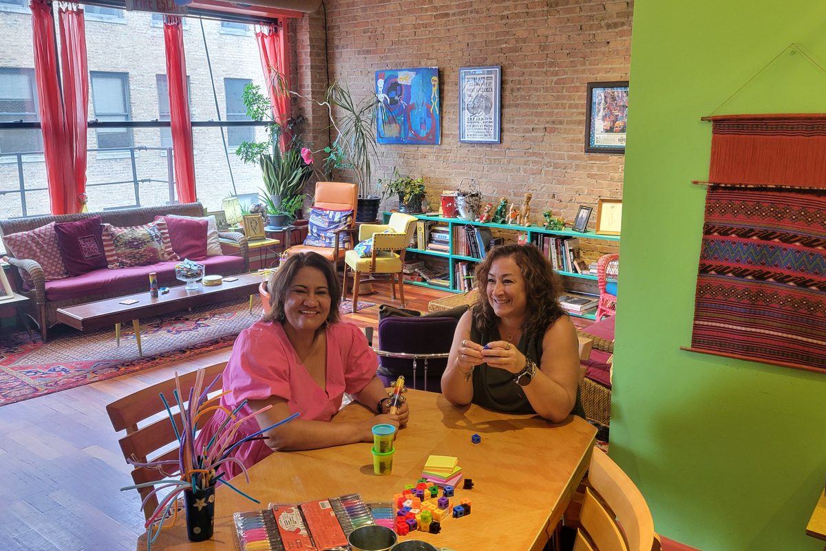 Two people in conversation across a worktable covered in
                      markers, building blocks and sticky notes during a
                      facilitated session.